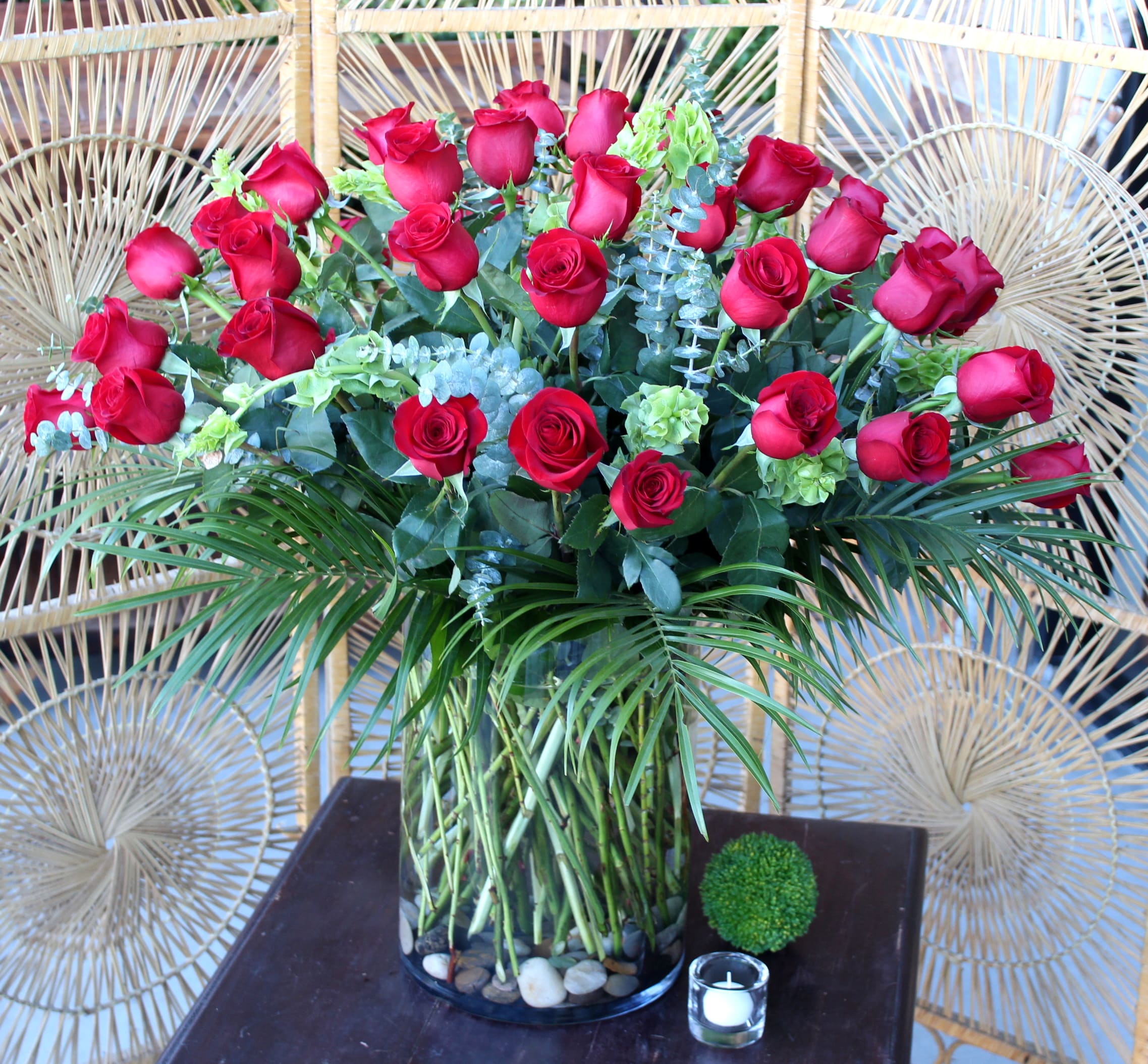 Red roses arranged in a clear glass vase with greenery and palm fronds