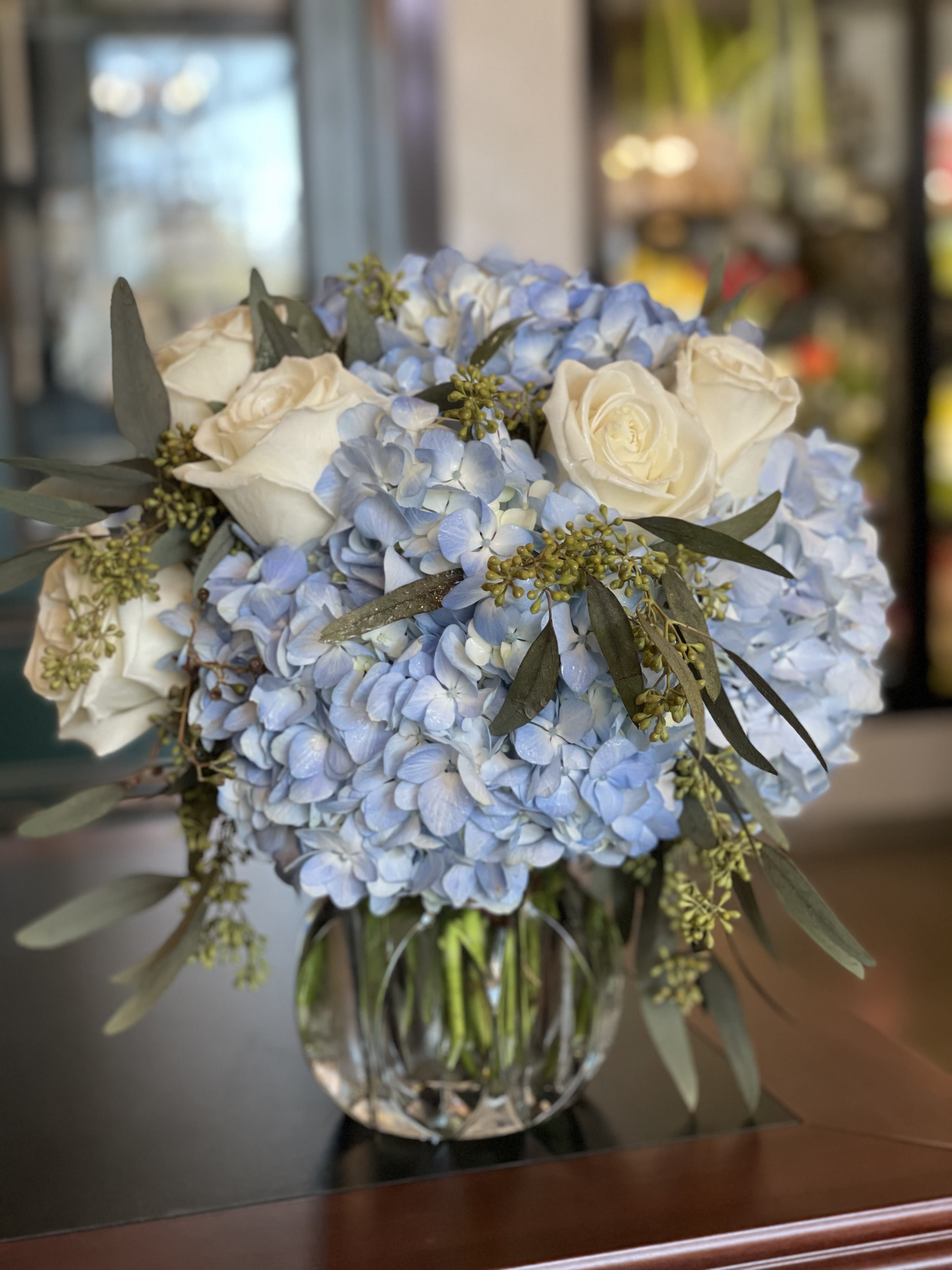 True Blue - A captivating blend of serenity and style. True Blue pairs lush blue hydrangeas with pristine white roses and soft, silvery dusty miller in a clear glass vase, creating a cool, timeless palette that suits any occasion—from heartfelt thank-yous to elegant celebrations.  Please note: Seasonal flowers may vary based on availability, ensuring each arrangement is unique and fresh.  Freshness Guarantee: We stand behind our quality. Your flowers are guaranteed to look fresh and beautiful for 3–5 days from delivery. To help them last:  •Top off the vase with clean water daily.  •Keep arrangements away from direct sun, heat, and drafts.  •Trim stems slightly after a couple of days if possible.