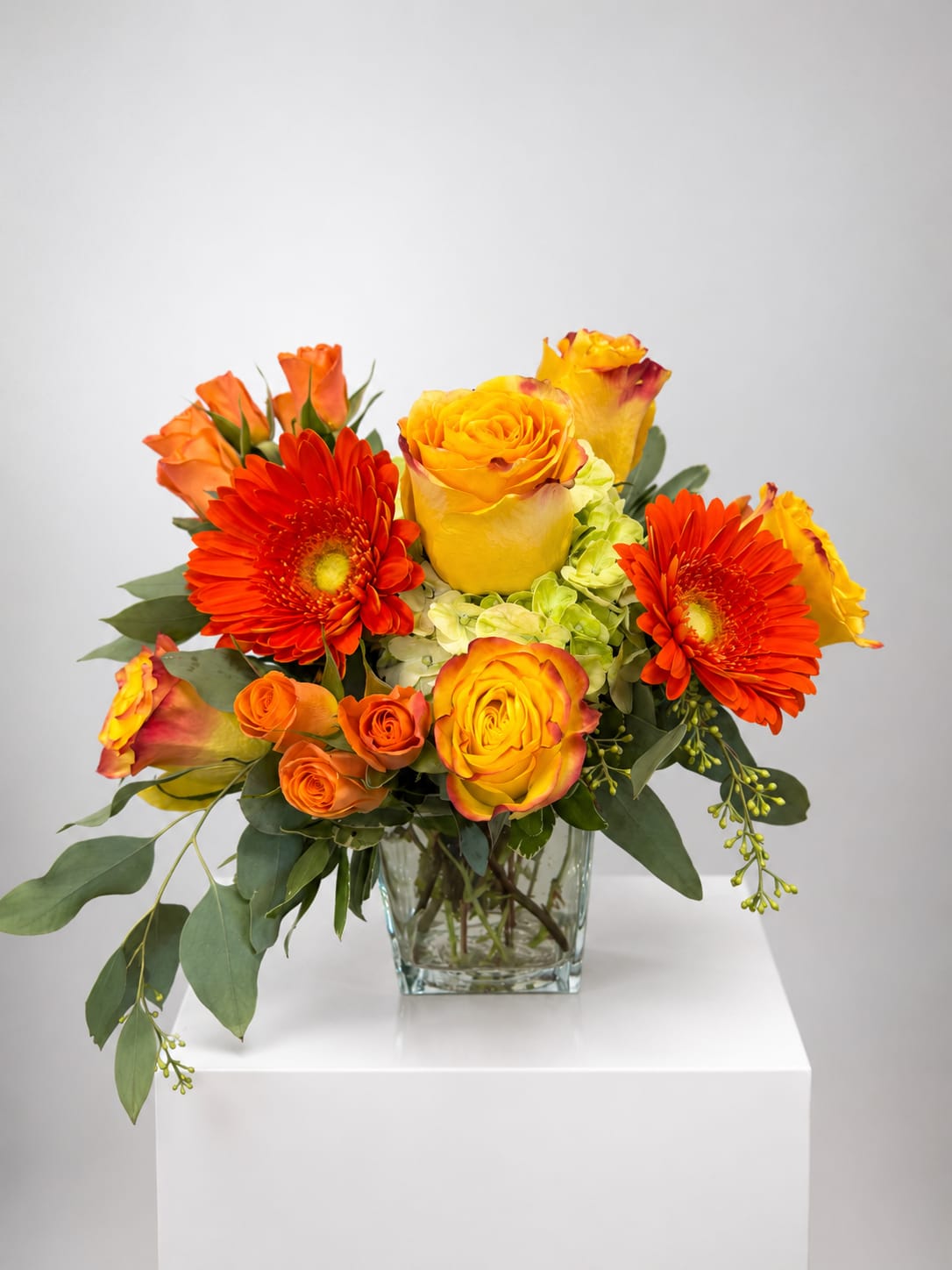 Orange and yellow roses with red gerbera daisies in a glass vase