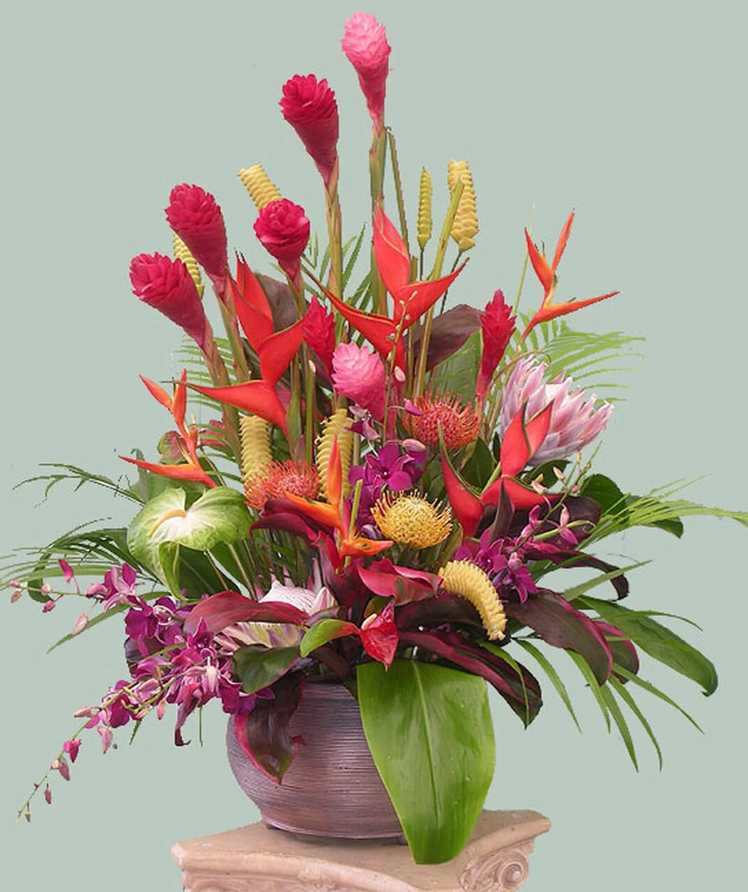 Tropical flower arrangement in a round vase with pink, red, and orange blooms