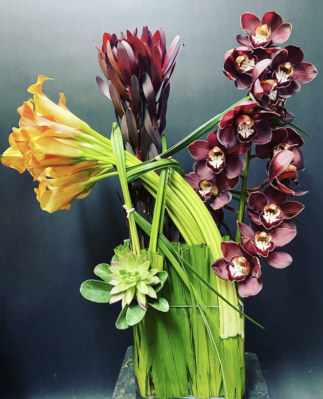 Arrangement of orchids, calla lilies, and a succulent in a tall vase