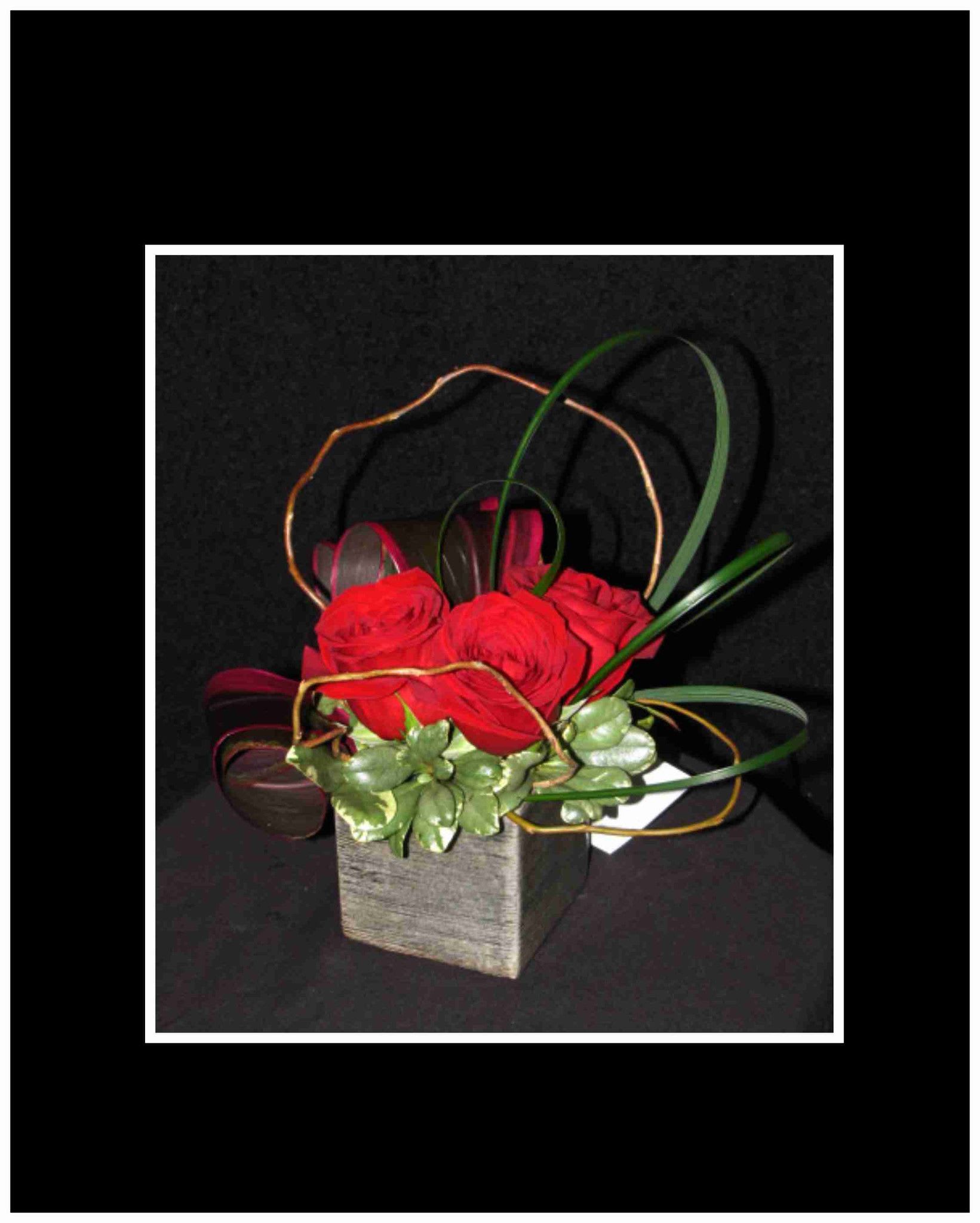 Red roses in a square vase with looping decorative reeds