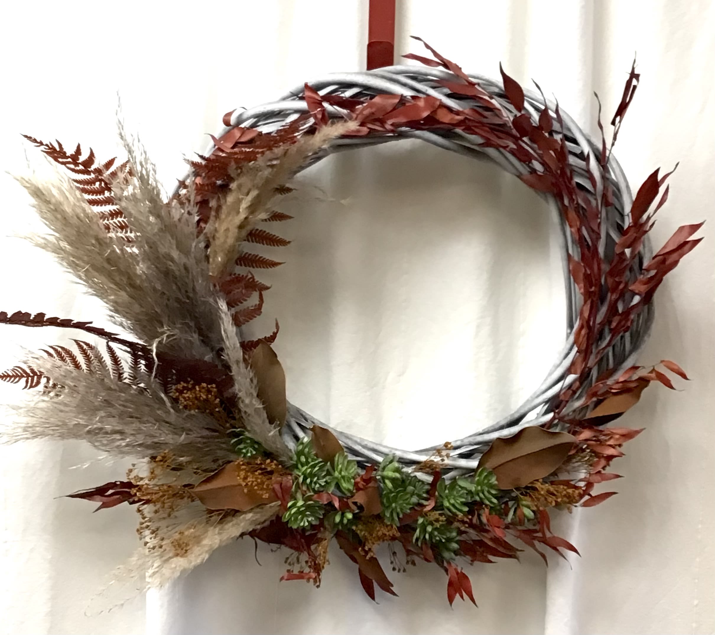 Decorative wreath with dried grasses and red foliage on a silver ring