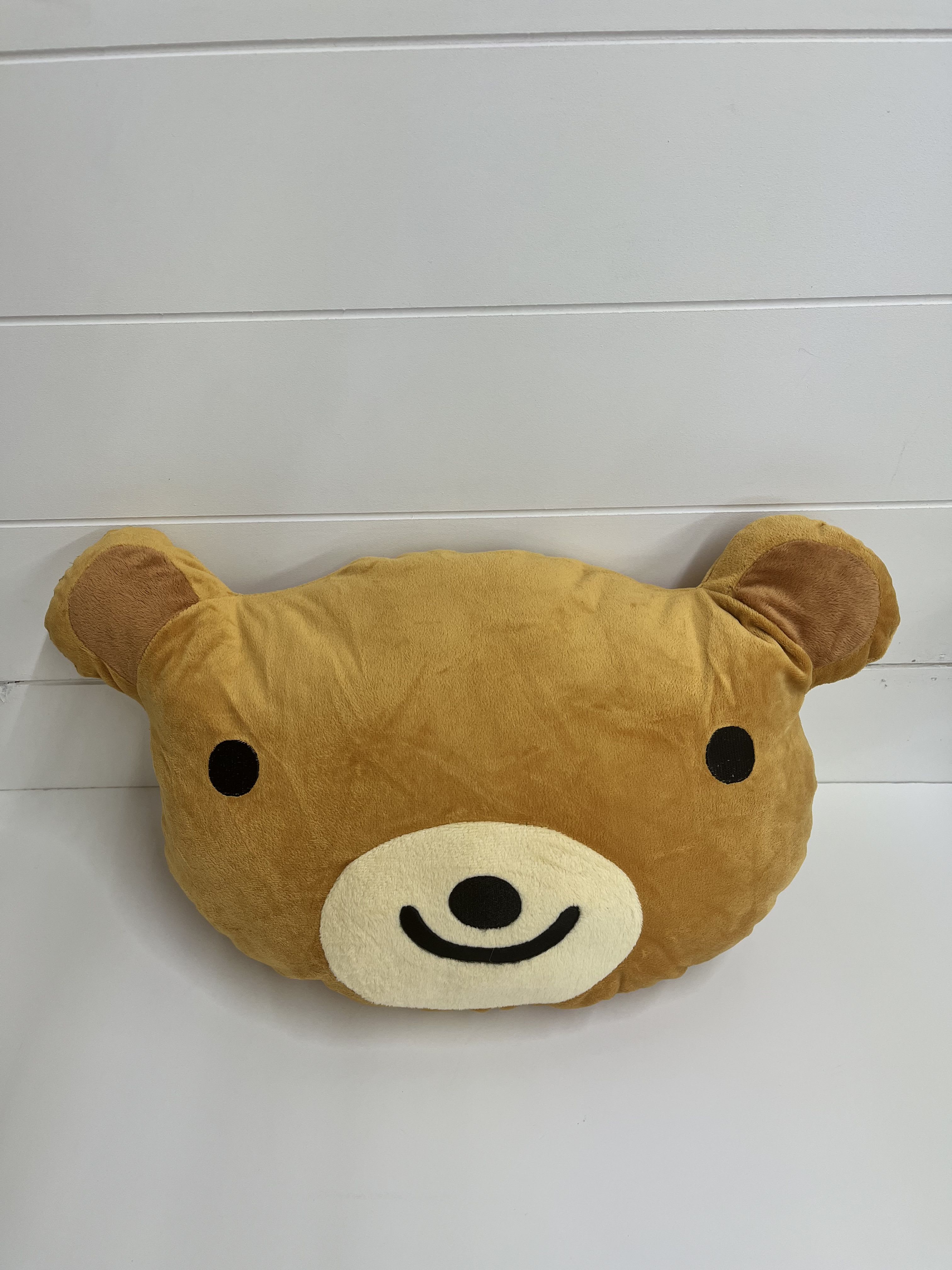 Brown teddy bear face plush pillow with black eyes and a smiling muzzle