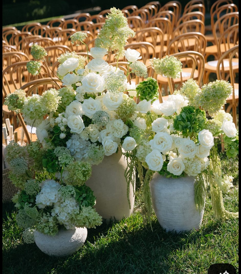 White rose and hydrangea arrangements in stone vases at outdoor wedding seating