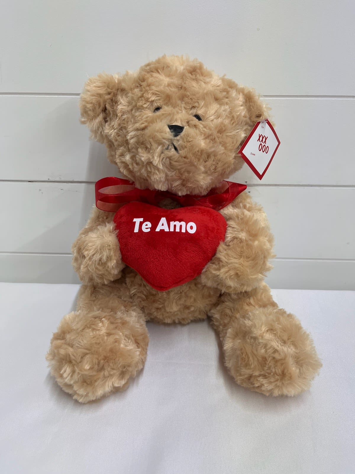 Tan teddy bear holding a red heart with the words "Te Amo" on a white surface
