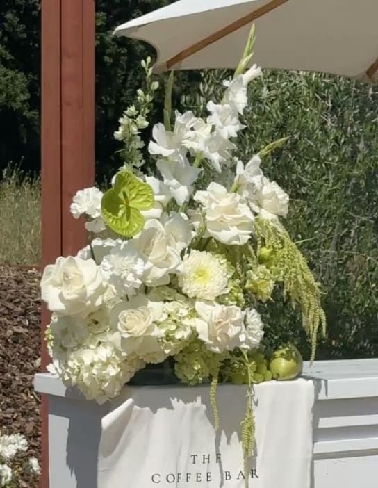 White floral arrangement with roses and orchids on a coffee bar table