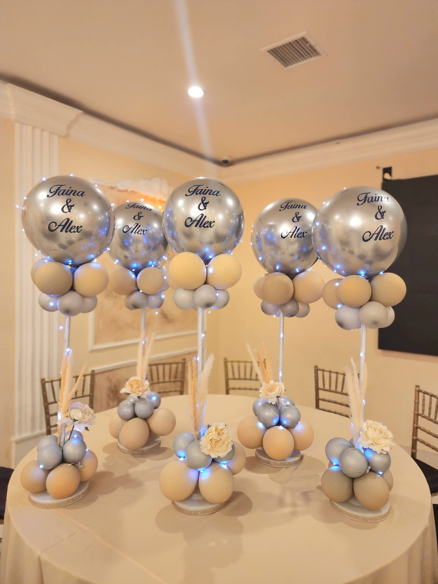 Silver balloons on stands with small cream floral accents on a table