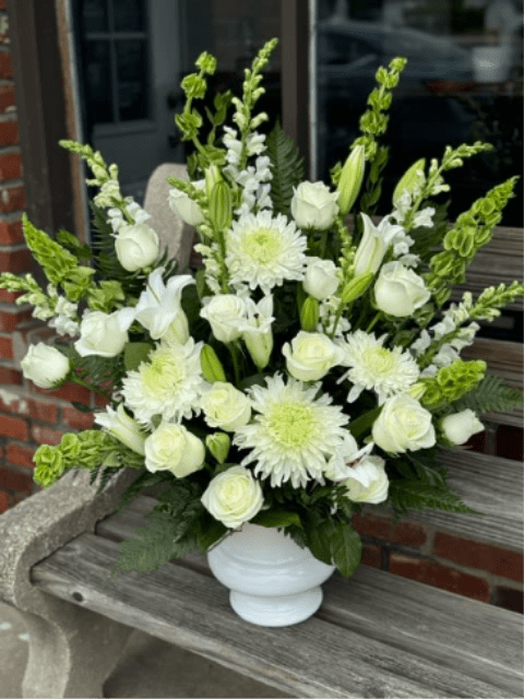 Serenity Urn Arrangement - Quiet beauty and a display of love for any funeral. Featuring white roses, lily, mums with bells of Ireland. 