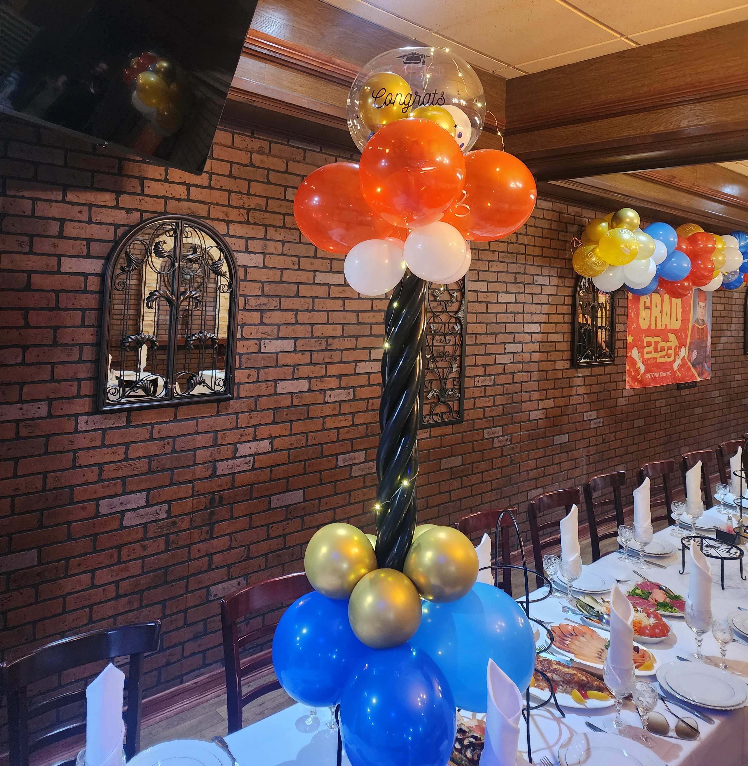 Balloon centerpiece with orange, blue, gold, and white balloons at a decorated table.