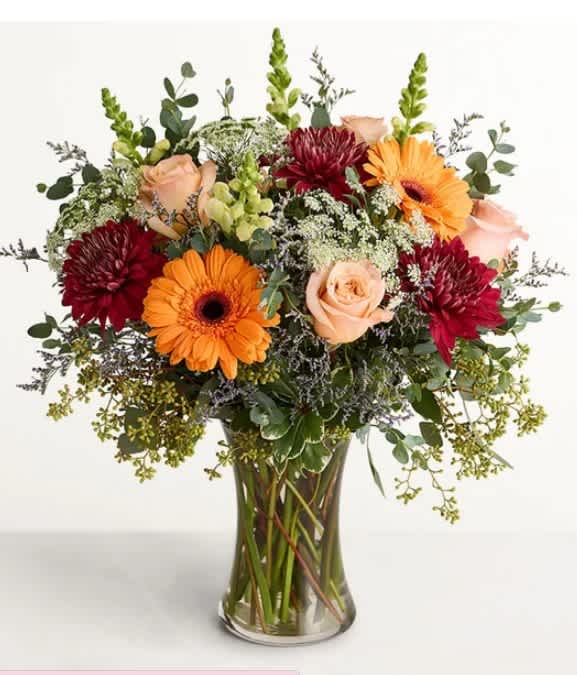 Mixed bouquet of orange gerbera daisies, peach roses, and burgundy blooms in a glass vase
