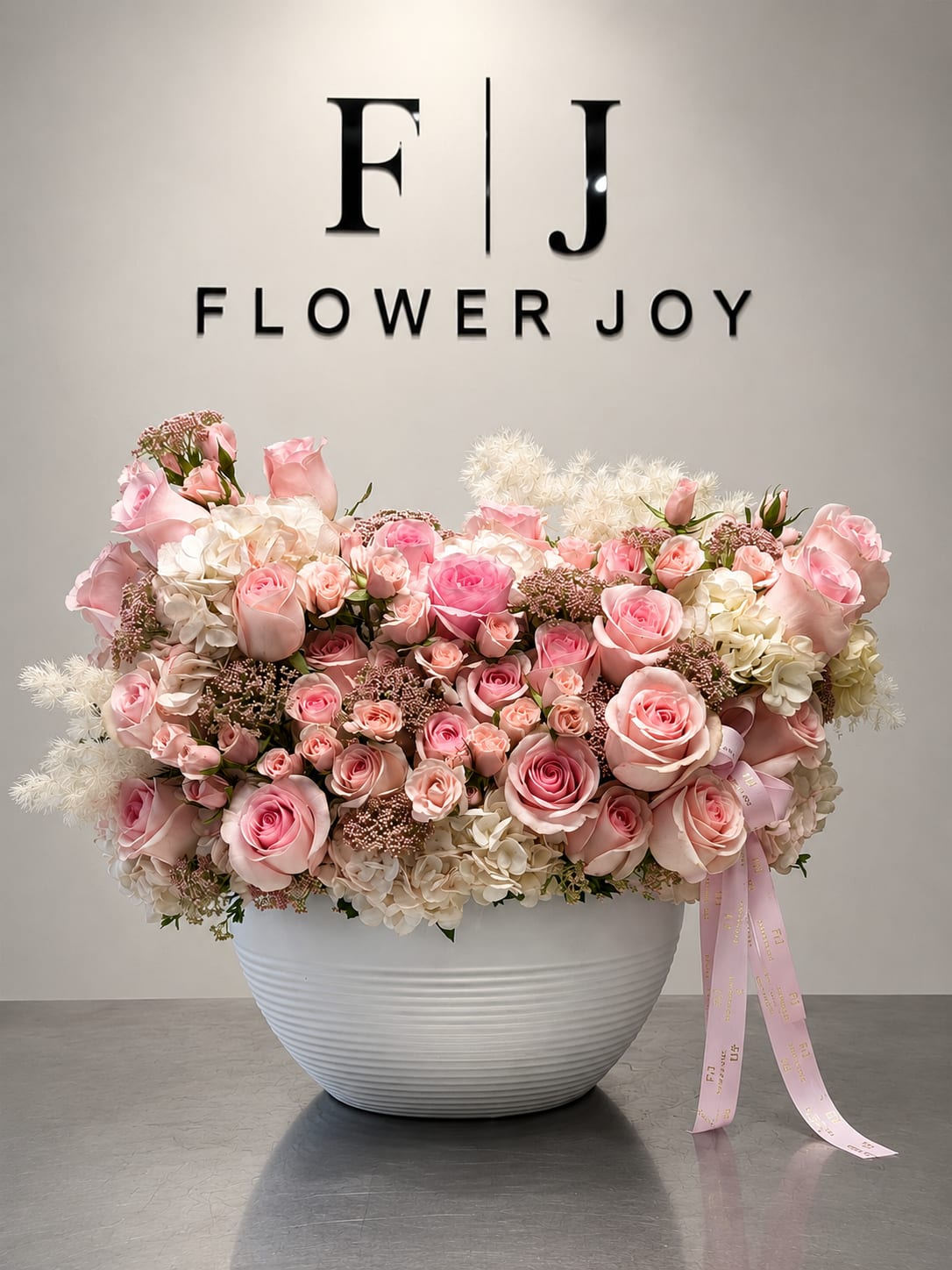 Pink and white rose arrangement in a white bowl vase with a ribbon