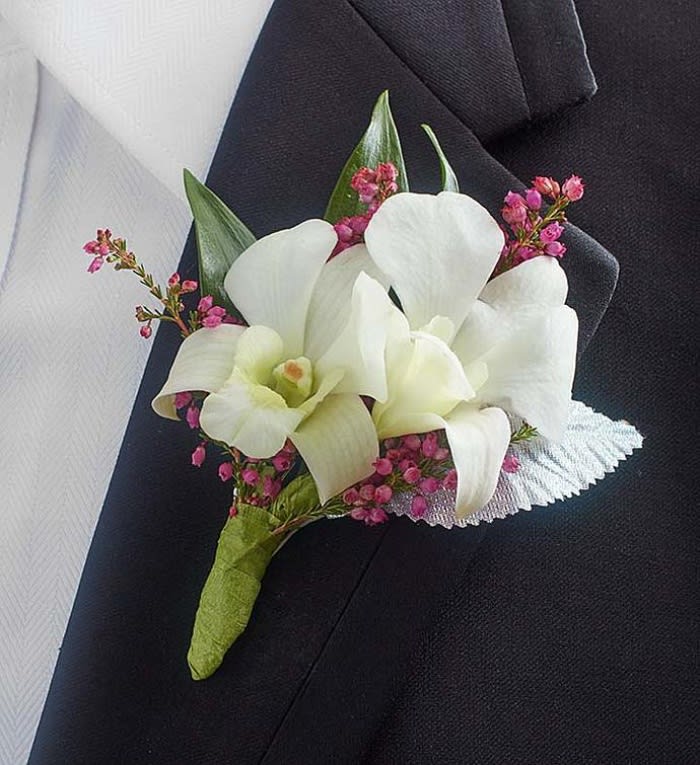 White orchid boutonniere with pink filler flowers on a dark suit lapel