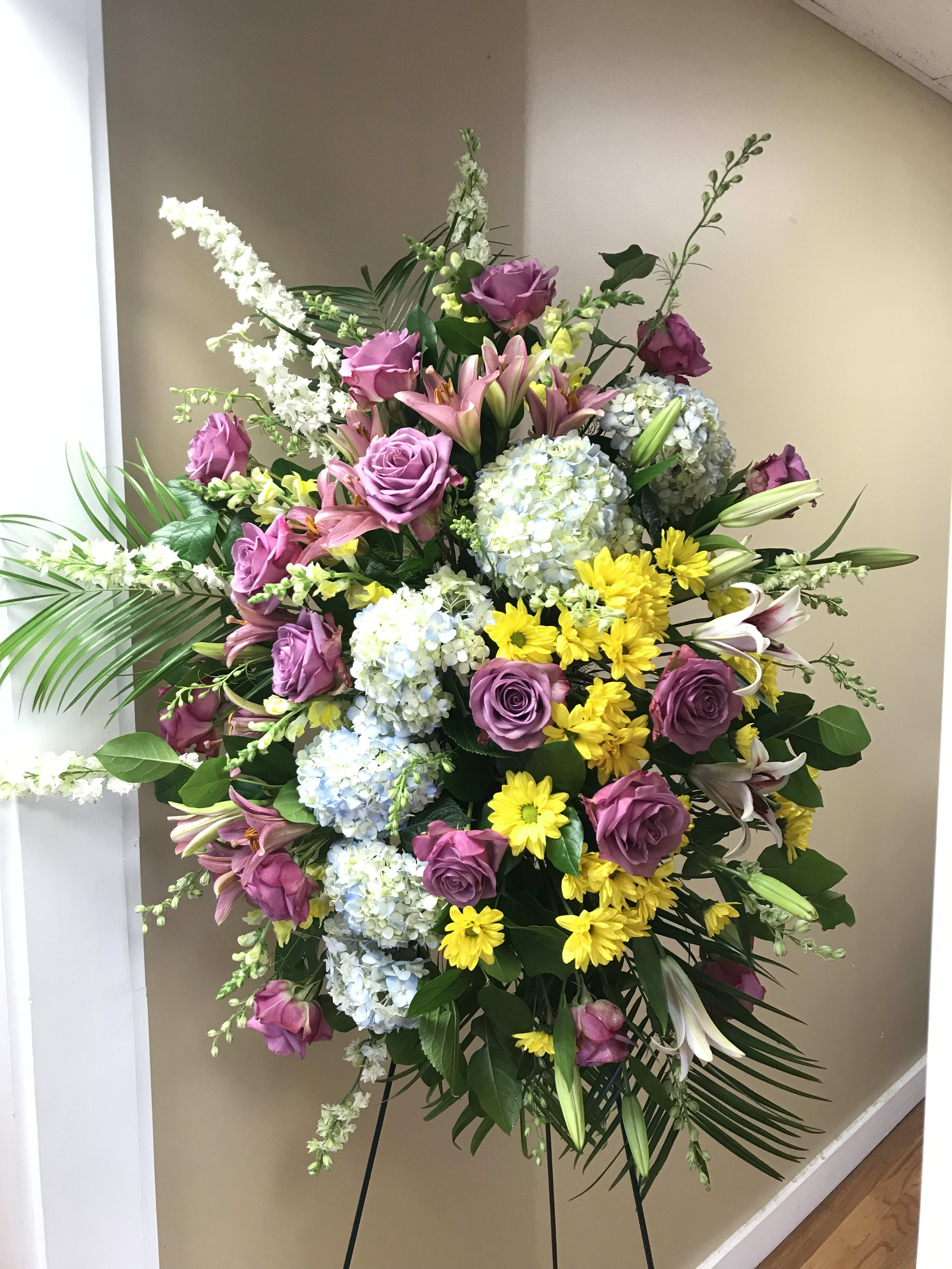 Standing floral spray with purple roses, lilies, hydrangeas, and yellow daisies