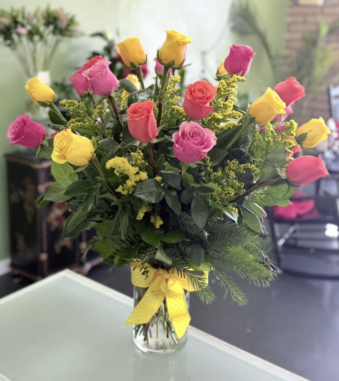 Bouquet of pink and yellow roses in a clear glass vase with a yellow ribbon