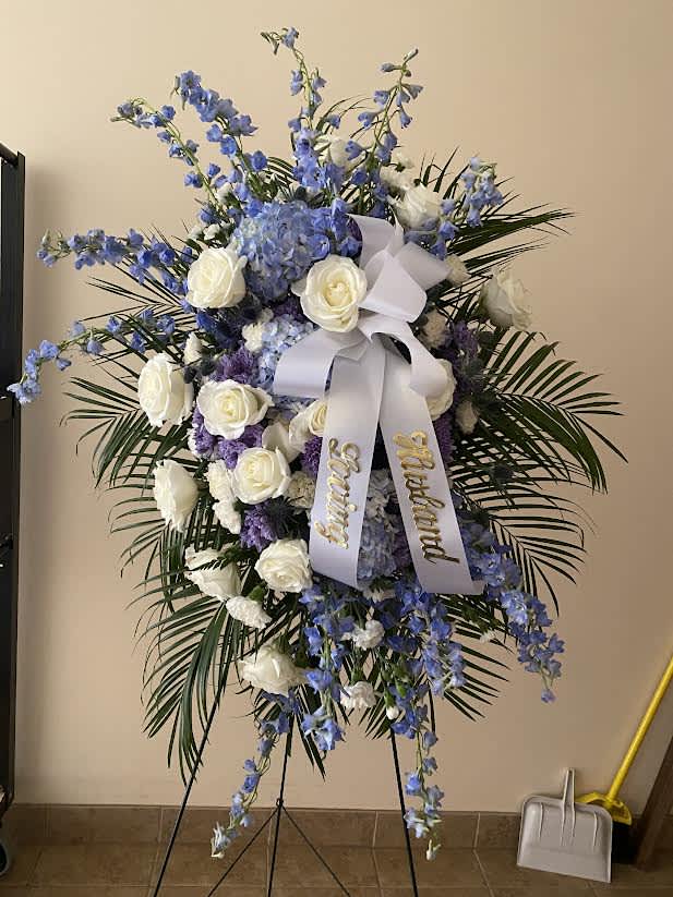 Standing floral spray with white roses, blue flowers, and a white ribbon