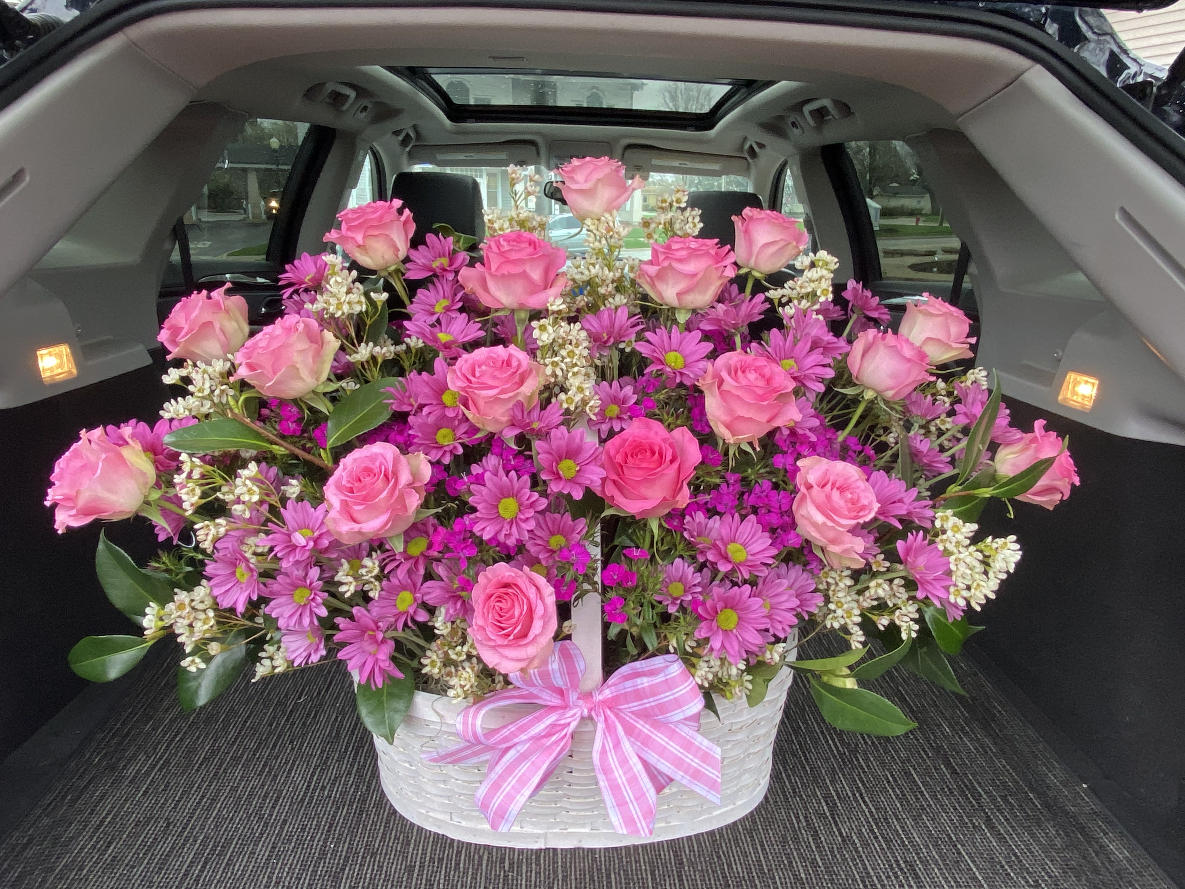 Pink roses and purple daisies arranged in a white basket with a pink ribbon