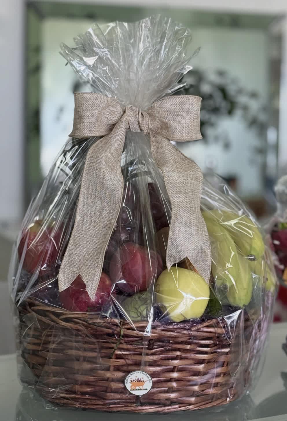 Wrapped fruit basket in a wicker container with a beige bow
