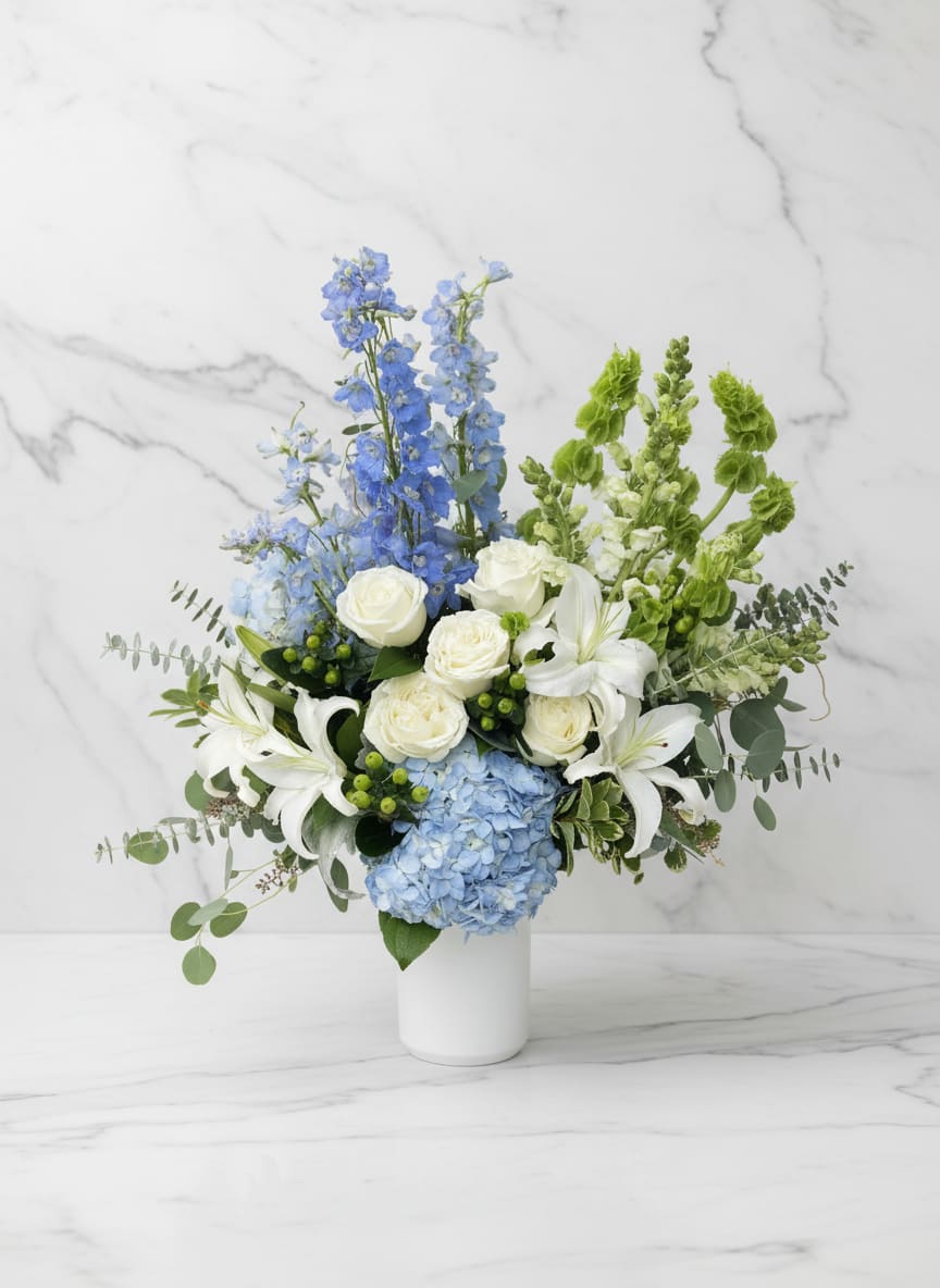 Pacific Mist - Soft and serene, Pacific Mist captures the tranquil beauty of the coast with blue hydrangeas, white roses, lilies, and lush seasonal greenery. The gentle palette and airy design evoke ocean breezes and quiet elegance — perfect for any occasion that calls for calm sophistication.  Handcrafted by Polk Street Florist in San Francisco, this refined arrangement brings a touch of coastal luxury to homes, events, and heartfelt gestures. Pictured in Premium