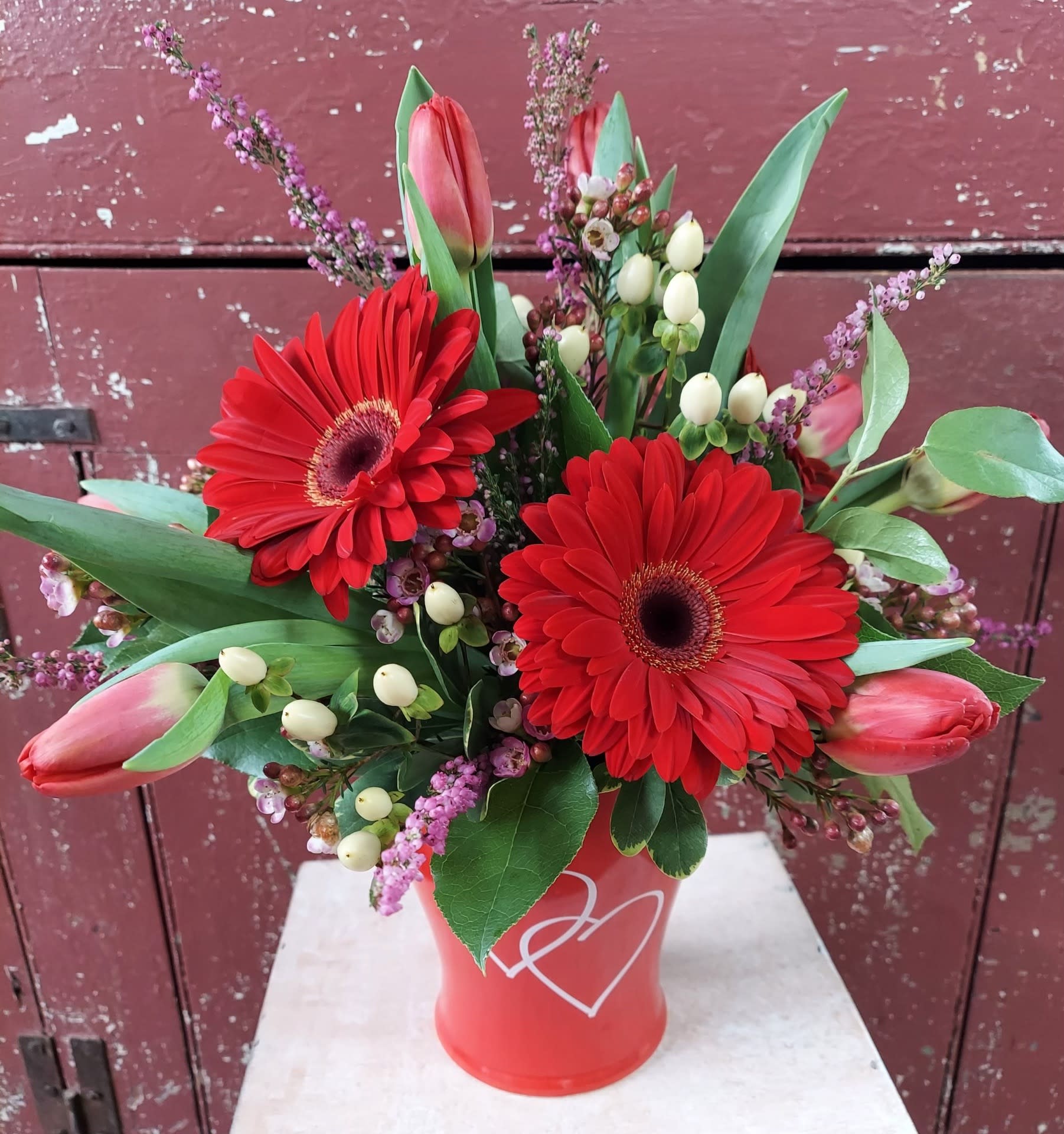 Red gerbera daisies and pink tulips in a red vase