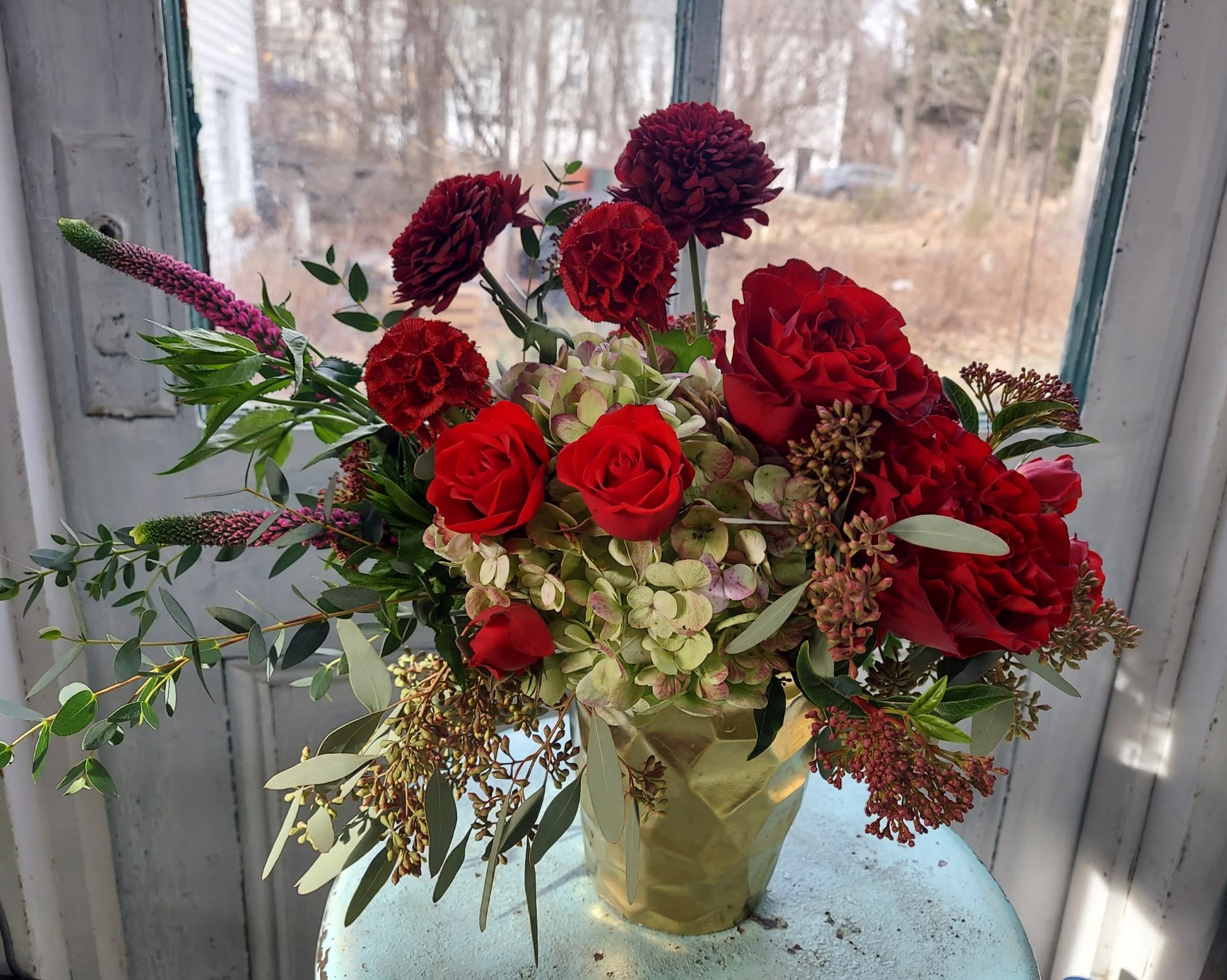 Red roses and burgundy blooms in a gold vase