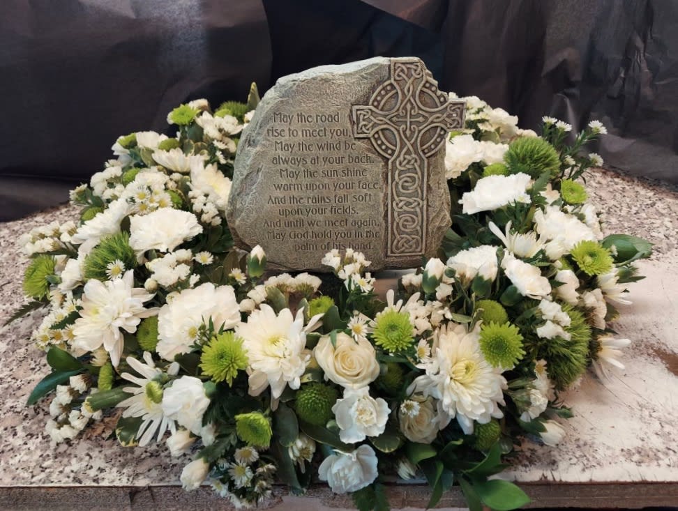 White floral wreath around a memorial stone with a Celtic cross