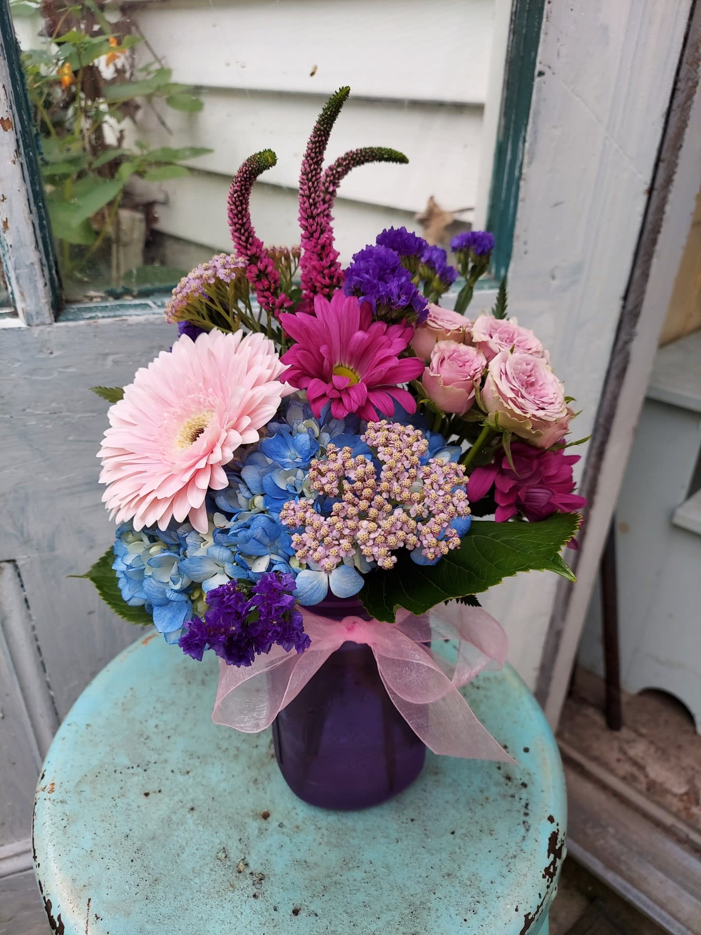 Colorful bouquet in a purple vase with a pink ribbon