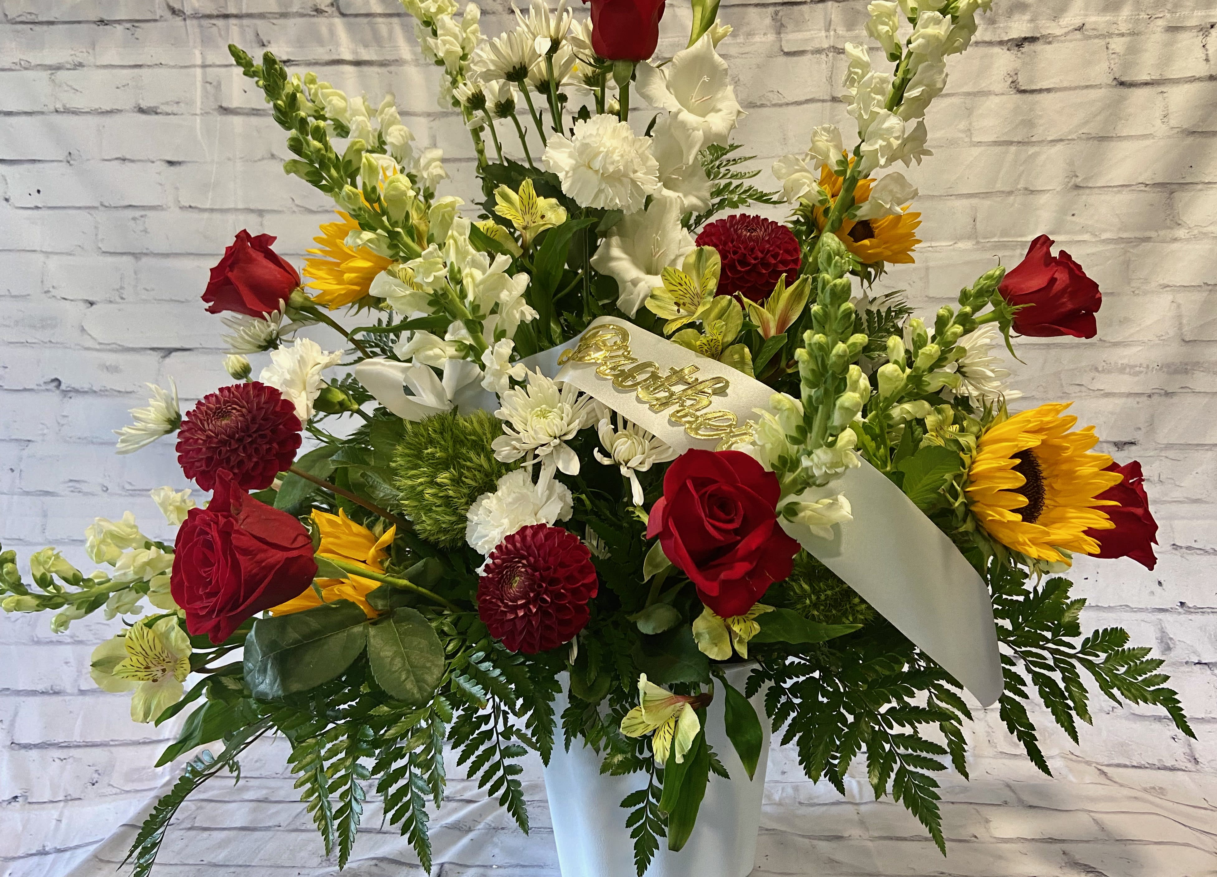 Red roses, sunflowers, and white flowers in a white vase with a ribbon