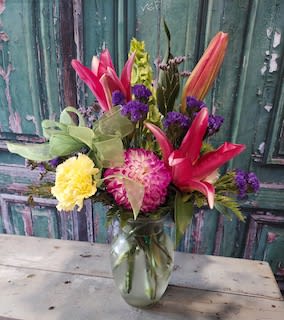 Mixed bouquet with pink lilies, yellow carnations, and purple flowers in a glass vase