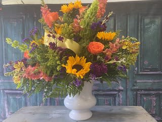Mixed bouquet in a white vase with sunflowers, roses, and purple blooms