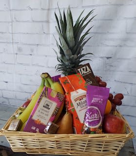 Fruit basket with a pineapple, bananas, grapes, and assorted packaged snacks
