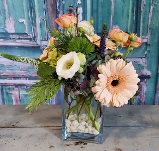Peach and white flowers arranged in a clear square vase