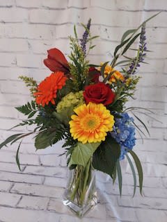 Mixed bouquet in a clear glass vase with red, yellow, orange, and blue flowers