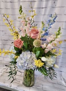 Mixed pastel bouquet in a glass vase with pink roses and blue hydrangeas