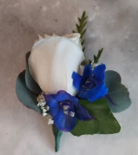 White rose boutonniere with blue flowers and greenery