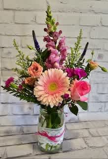 Mixed pink and peach flowers in a glass jar vase with a ribbon