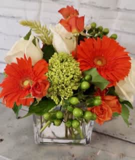 Orange gerbera daisies and white roses in a clear square vase