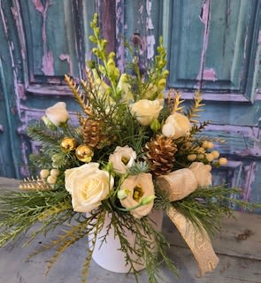 Cream roses and white blooms arranged in a white vase with pinecones