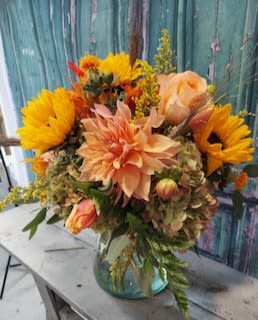 Bouquet of sunflowers, peach dahlias, and roses in a glass vase
