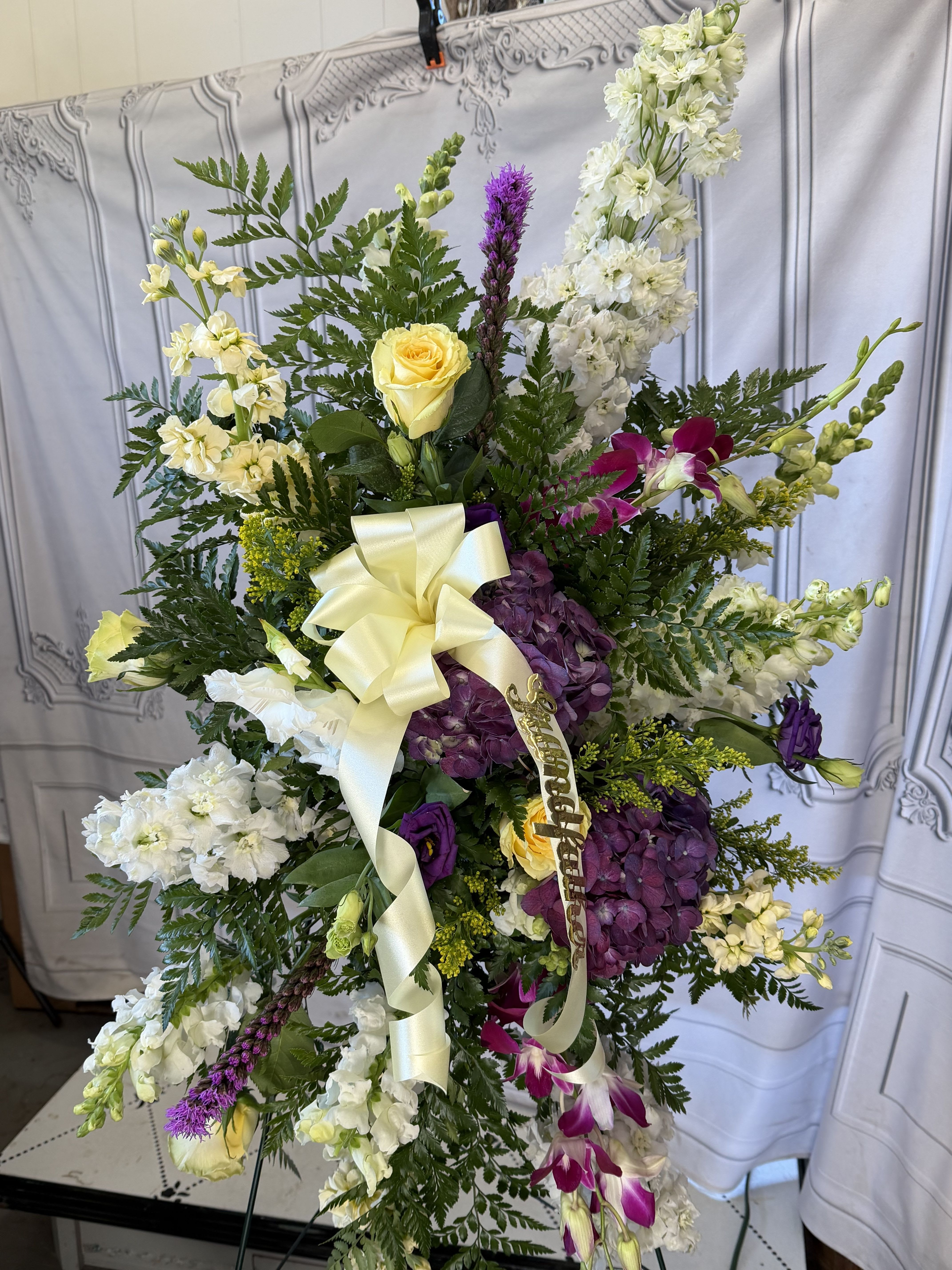 Standing floral spray with white, purple, and yellow blooms and a cream ribbon