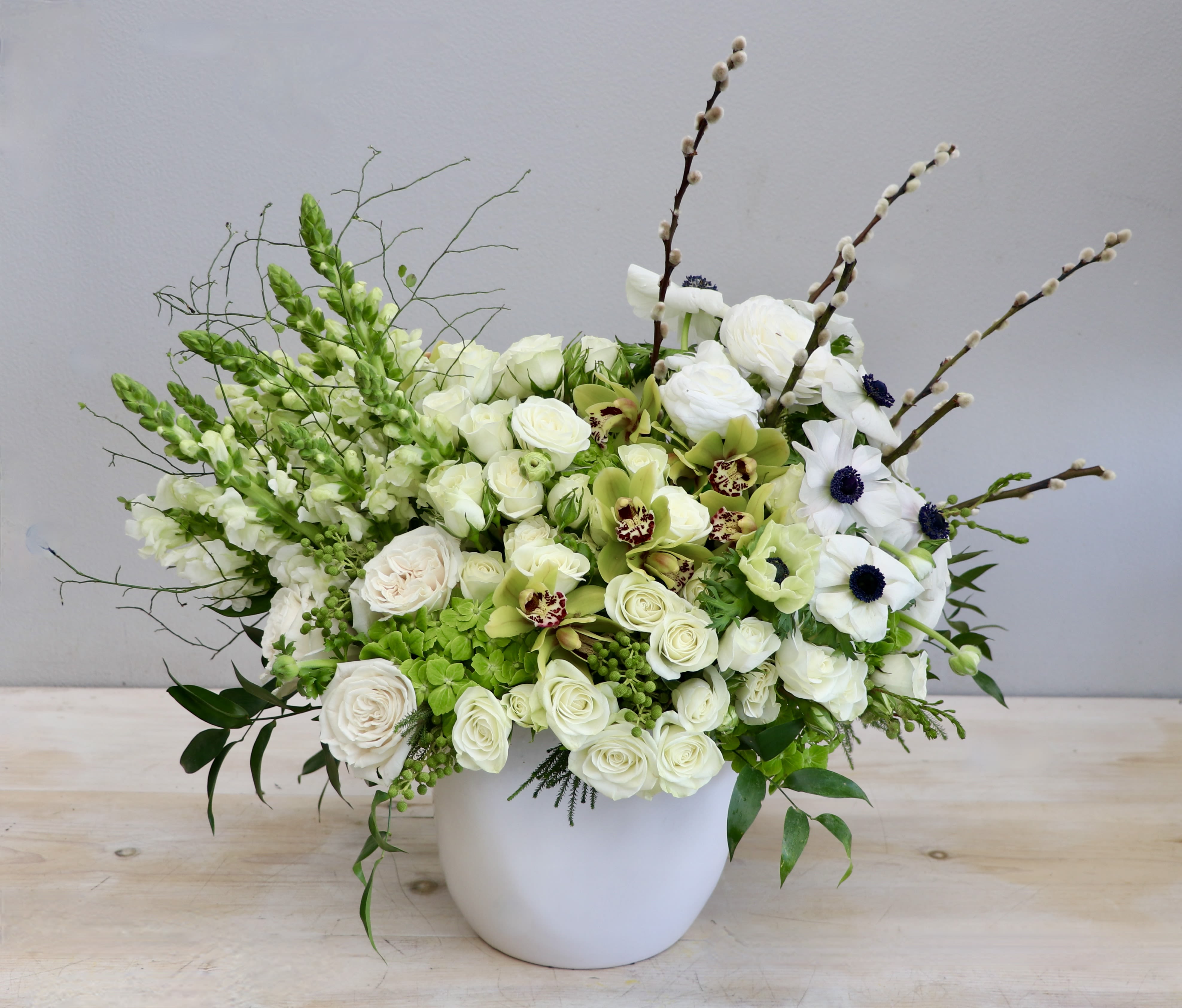 Asymmetrical white and green floral arrangement in a white ceramic pot