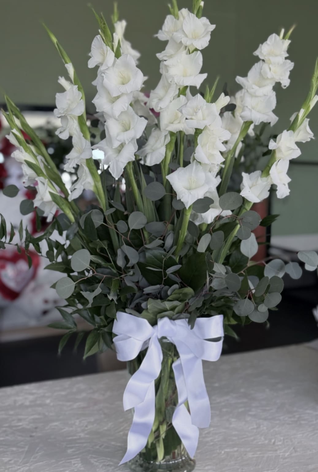 White gladiolus arrangement in a clear glass vase with a white ribbon