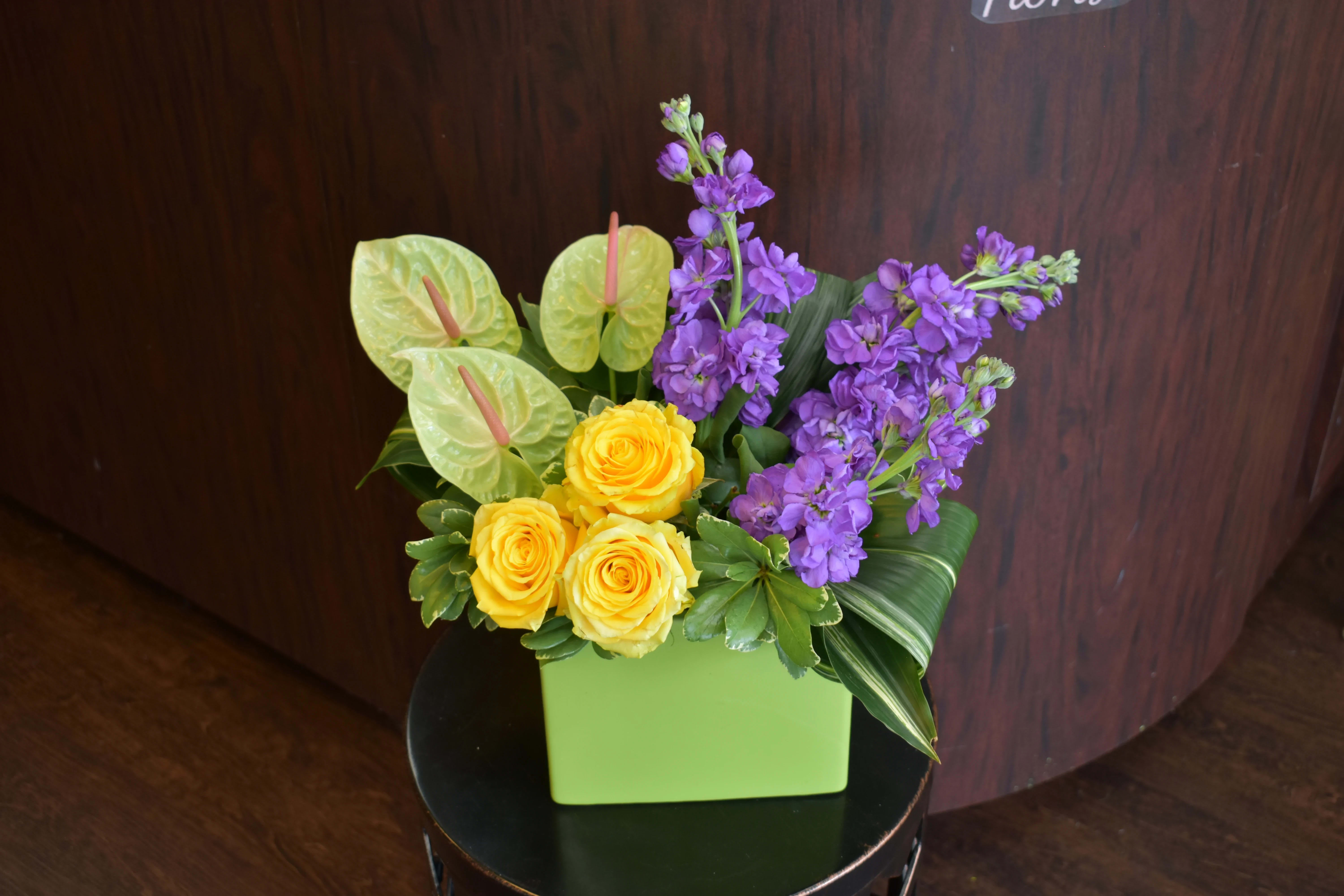 Yellow roses and purple flowers in a green square vase