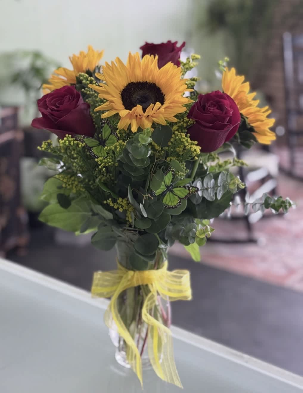 Bouquet of sunflowers and dark red roses in a glass vase