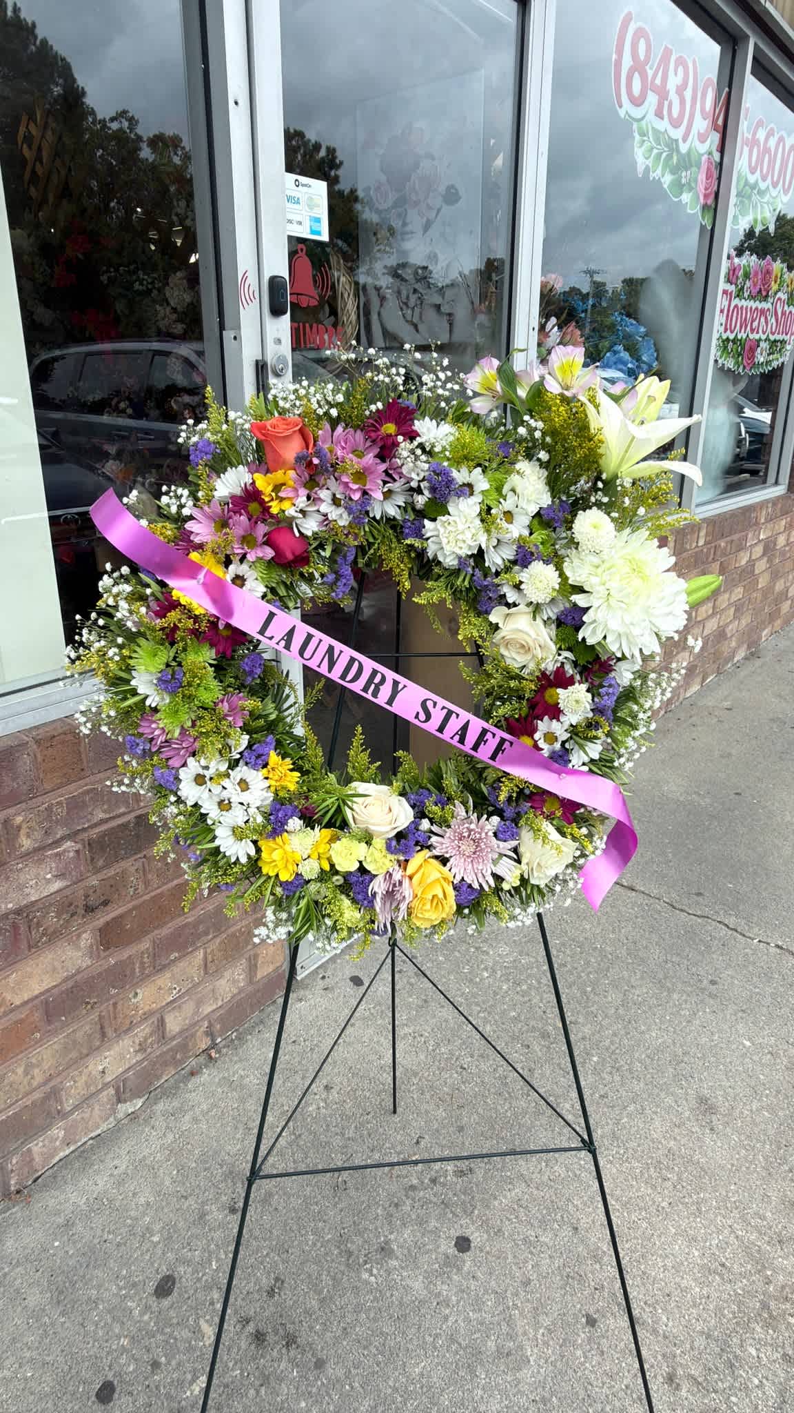 Large floral wreath on a stand with a pink ribbon reading "LAUNDRY STAFF"