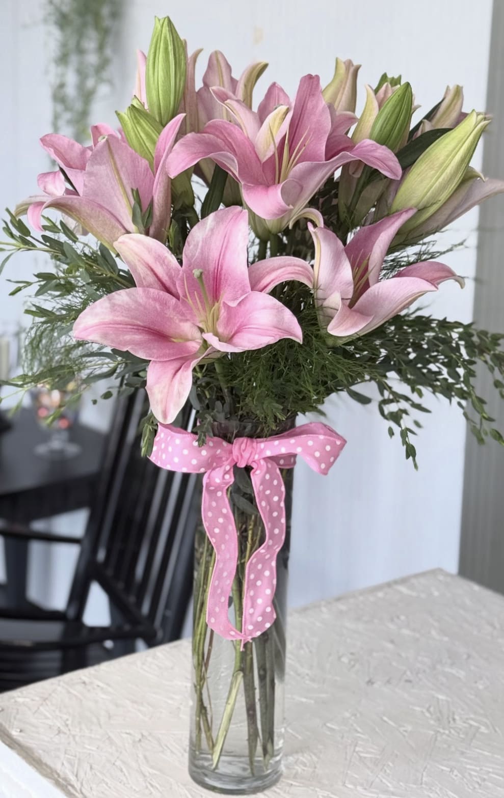 Pink lilies in a clear glass vase tied with a pink polka-dot ribbon.