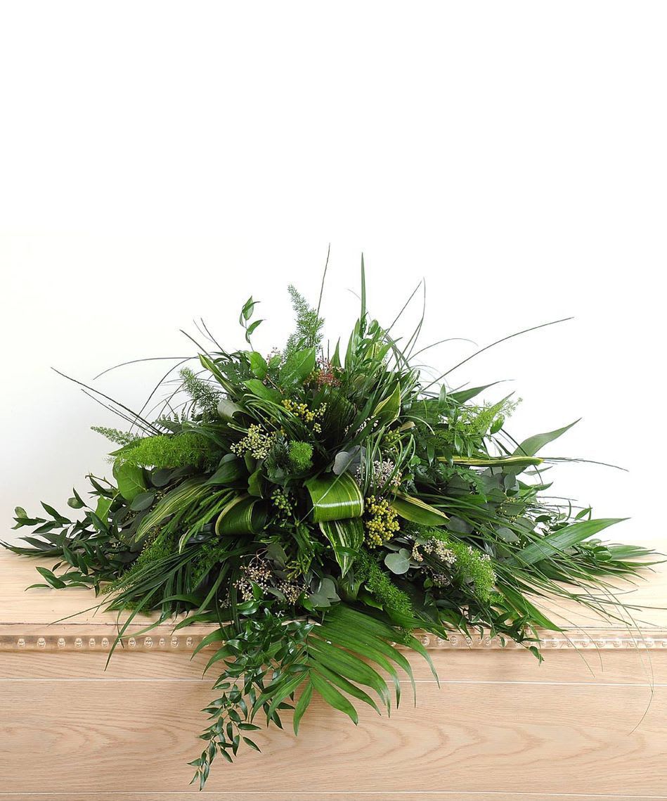 Large low arrangement of assorted green foliage on a wooden casket
