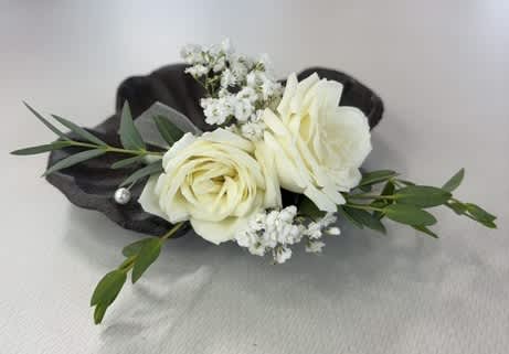 White rose boutonniere with small white filler flowers and dark green leaves