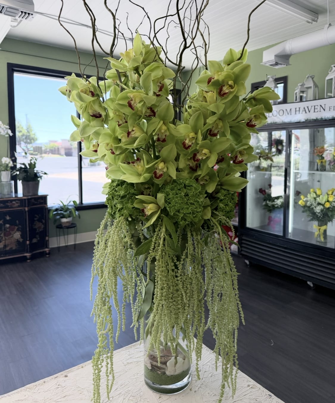Tall arrangement of green orchids with trailing greenery in a glass vase