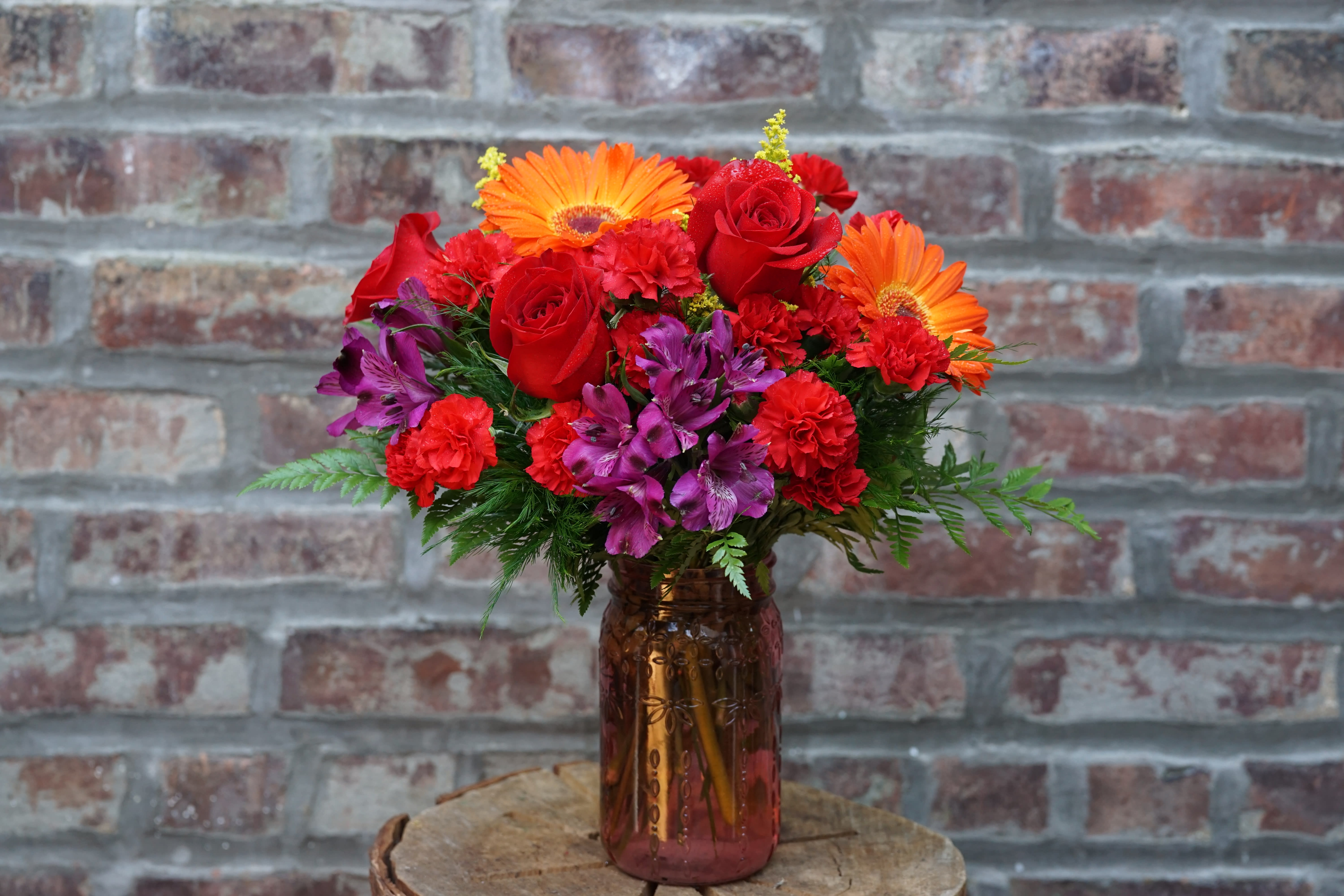 Bouquet of red roses, orange gerbera daisies, and purple flowers in a glass vase